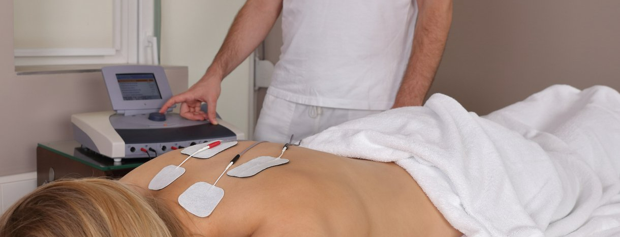 A person receives electrical stimulation therapy on their back while lying on a massage table.