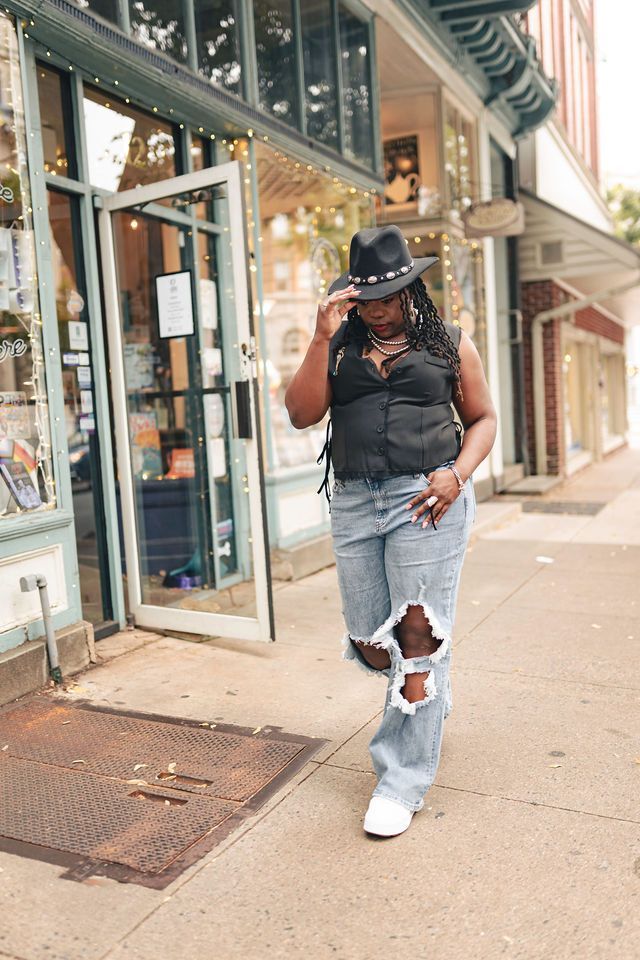 Woman in cowboy hat and ripped jeans walks past a storefront.