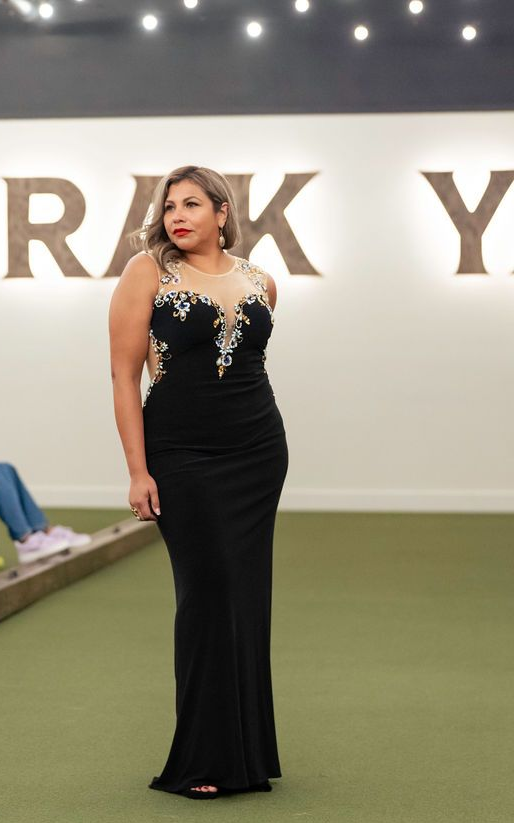 Woman in a black evening gown, standing on a green surface with white background and large letters.