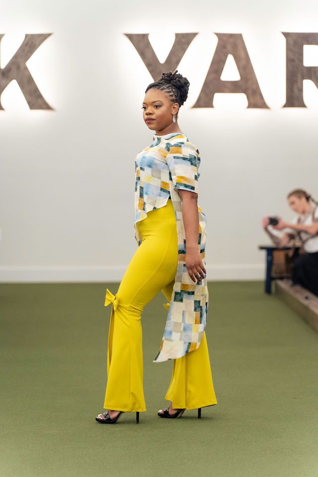 Woman modeling yellow flared pants and patterned top on a runway.