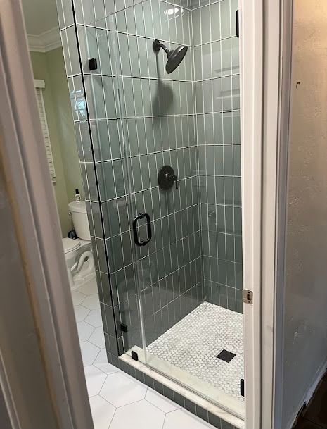 Modern shower with glass door and green tiled walls, set in a bathroom with white floors.