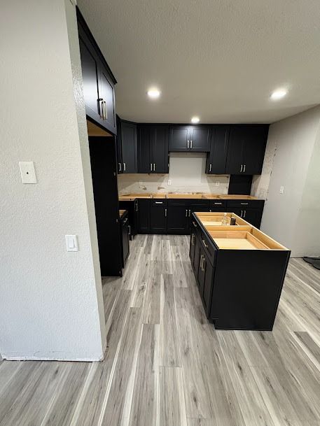 Black kitchen with island, light wood countertops, and gray flooring.