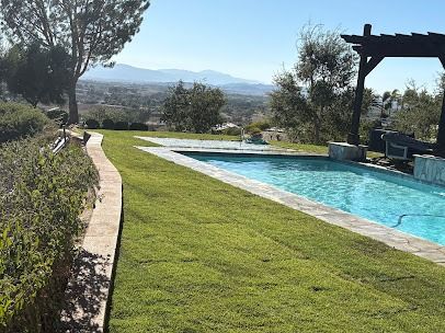 Poolside view with pool, green lawn, distant mountains and a pergola.