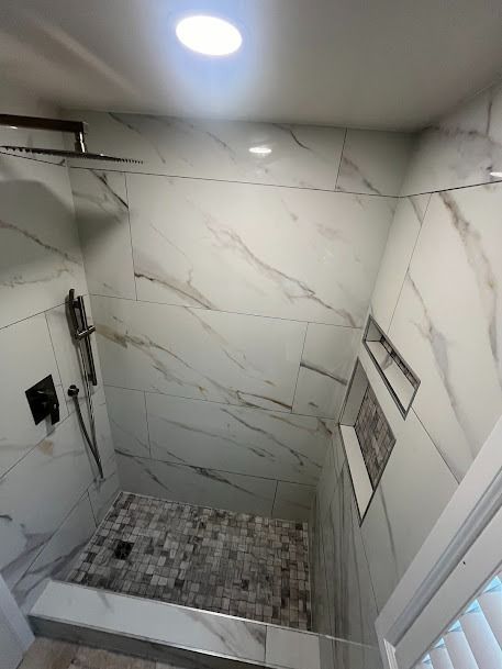 A newly tiled shower with marble-like white walls, a gray tiled floor, and recessed shelves.