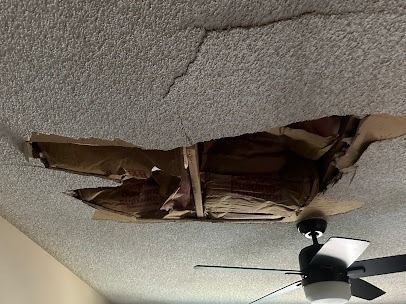 A ceiling with a large hole and cracks, near a ceiling fan.