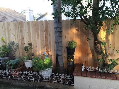 Wooden fence with potted plants, small white picket fence and a tree in a backyard.