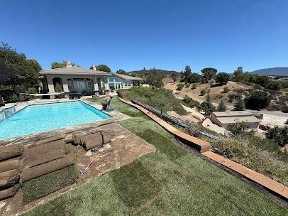 A large house with a pool and newly laid grass, overlooking a hilly landscape on a sunny day.