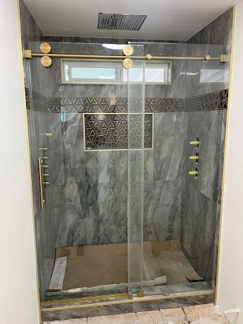 Shower with gold hardware, sliding glass doors, gray marble-look tile, and decorative accents.
