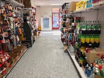 A convenience store aisle with shelves of products on both sides; a white door is at the end of the aisle.