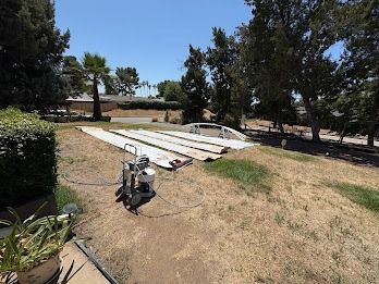 A paint sprayer next to white fabric sheets on a grassy slope with trees and a sunny sky.