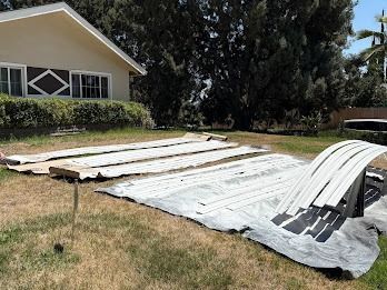 White trim pieces laid out on tarps in front of a house, preparing for painting.