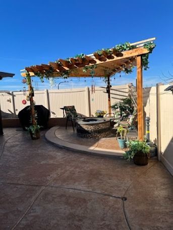 Patio with a pergola, fire pit, and seating on a sunny day. Faux greenery adorns the structure.