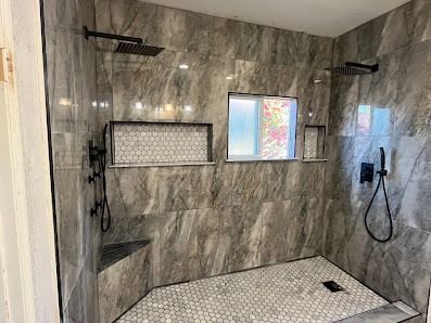 Modern shower with gray tile, black fixtures, and small window. Includes built-in shelves and a bench.