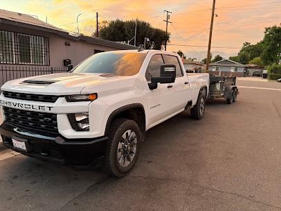 White Chevy pickup truck towing a trailer on a street at sunset.