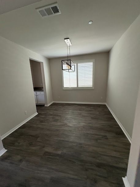 Empty dining room with wood-look floor, window with blinds, and hanging light fixture.