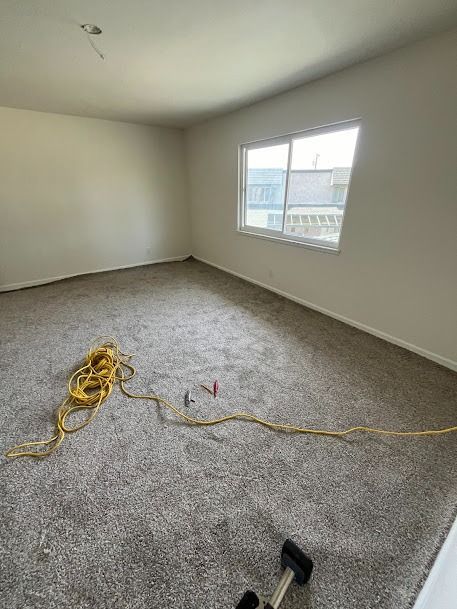 Room with gray carpet, white walls, window, and a yellow extension cord.
