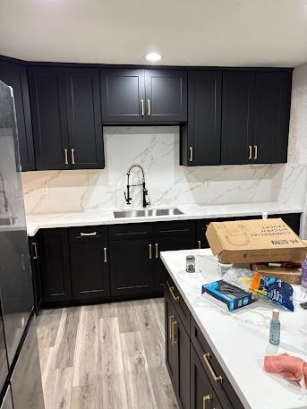 Black kitchen cabinets with white countertops, sink, and island. Light gray flooring.