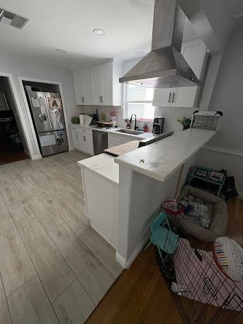 White kitchen with light wood floors, stainless steel appliances, and a breakfast bar.