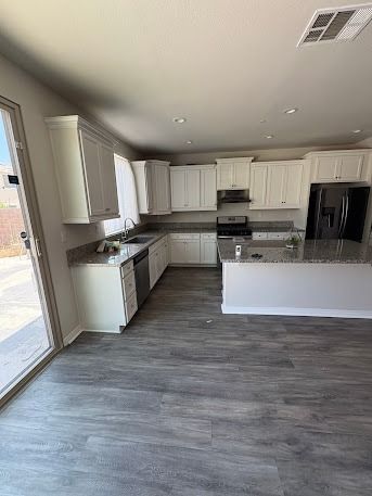 White kitchen with gray countertops and flooring.  Black fridge, stainless steel appliances. Sliding glass door.