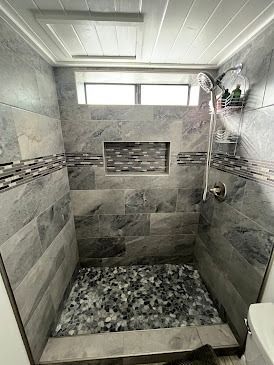 Gray tiled shower with stone floor, built-in shelf, and chrome showerhead.