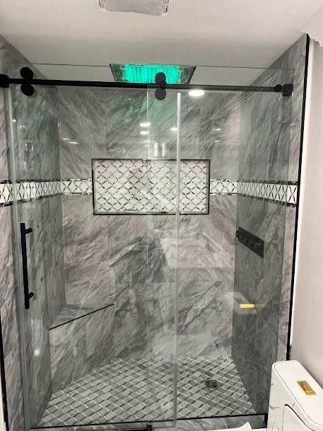 A modern, gray-tiled shower with a glass door, black hardware, and decorative tile in the center.