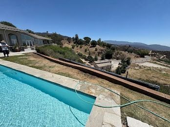 A long, blue pool in front of a house with a hillside view on a sunny day.