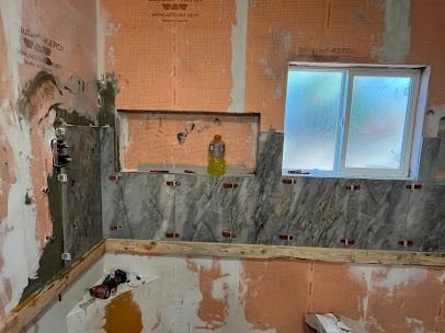 Bathroom renovation in progress: orange waterproofing membrane on walls, gray stone tiles, window, niche, bottle.