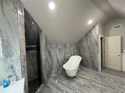 Modern bathroom with a freestanding tub and a glass shower. Gray and blue marble-like tiles and a white door.