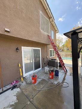 A tan house exterior has a ladder and buckets on the ground.