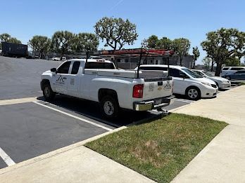 White work truck parked in a parking lot, next to a grassy area, under a bright blue sky.