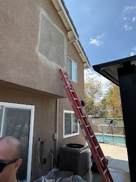 Ladder against house; patched stucco, near windows, person at base, pool in background.