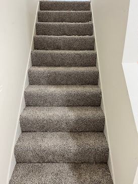 Gray carpeted staircase with white walls, viewed from below.