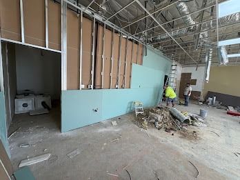 Construction site. Workers installing drywall on a wall. Interior space with unfinished ceiling and debris.