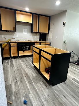 Kitchen under construction with black cabinets, unfinished interior, and island; grey flooring.
