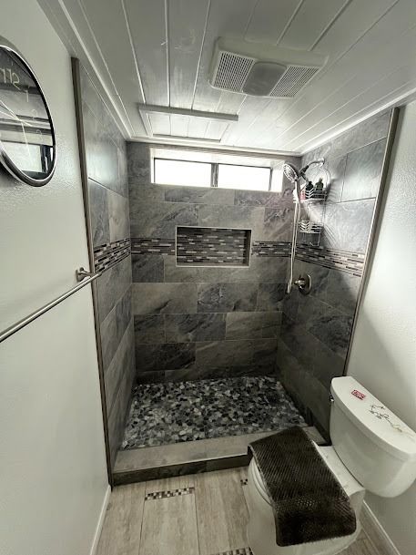 A bathroom with a stone-tiled shower and pebble floor, small window, and toilet.