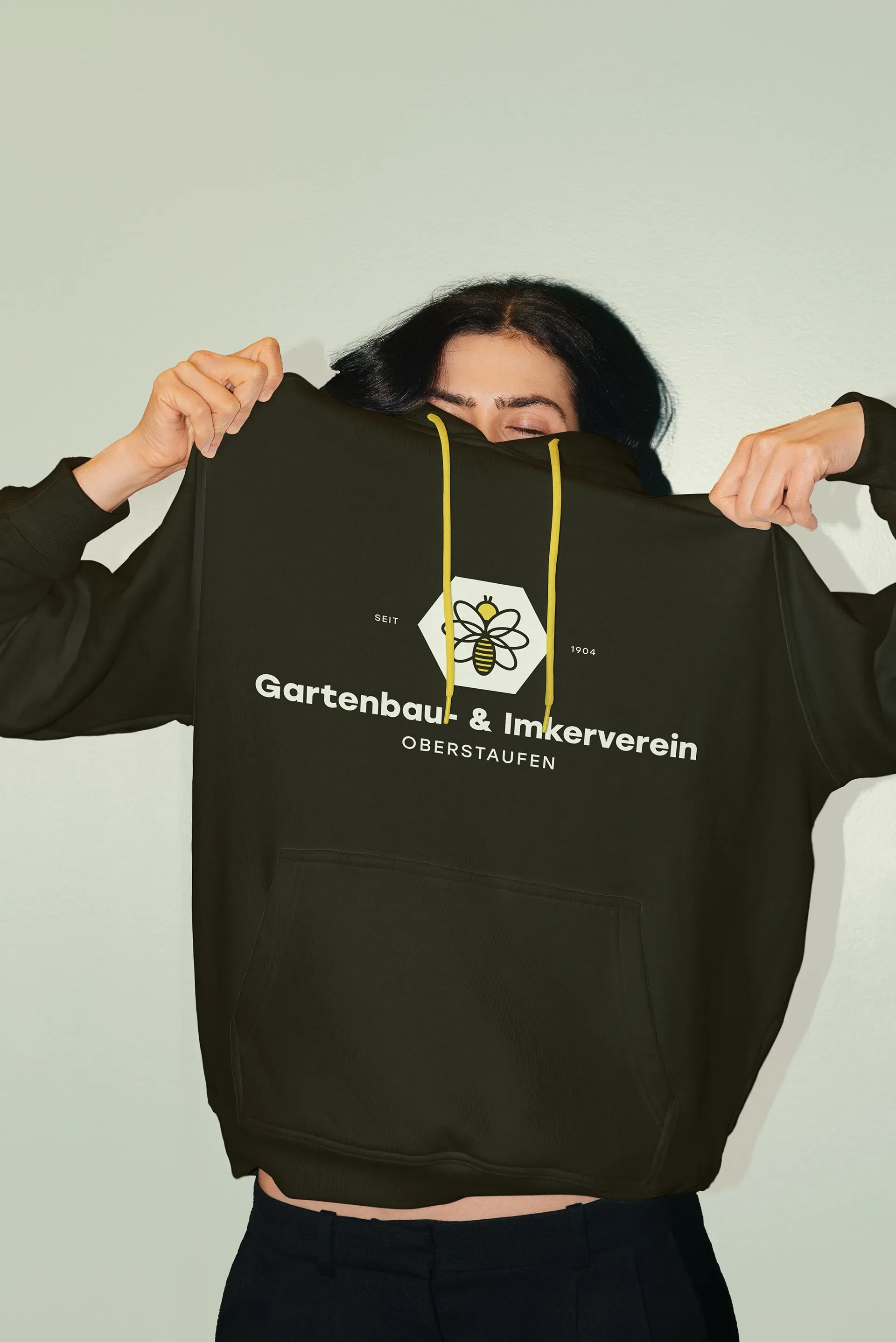 Eine Frau hält einen schwarzen Kapuzenpullover mit einer Biene darauf hoch.