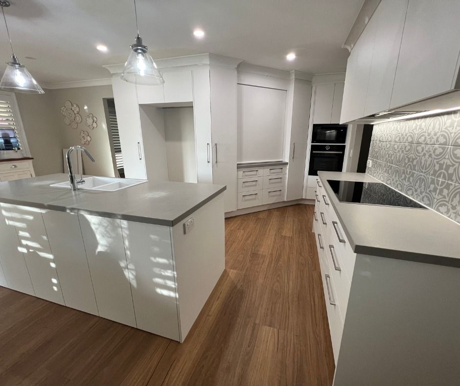 Modern White Kitchen With Island, Cabinets, and Wooden Floors — Nyblad Construction in Caloundra West, QLD
