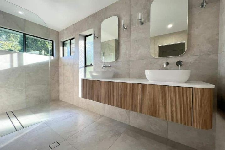 A Large Bathroom With Two Sinks And Mirrors And Floating Cabinet — Nyblad Construction in Caloundra West, QLD