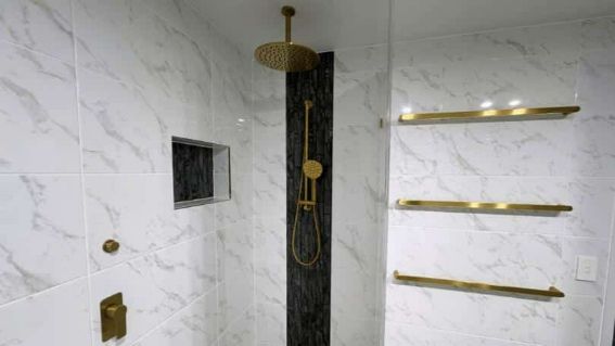 A Bathroom With Marble Tiles And A Walk-In Shower With A Gold Shower Head — Nyblad Construction in Caloundra West, QLD
