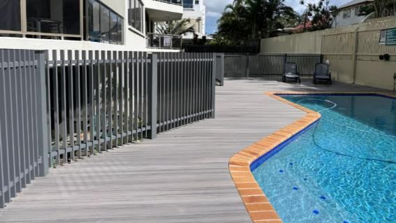A Fence Surrounds A Swimming Pool With A Wooden Deck — Nyblad Construction in Caloundra West, QLD