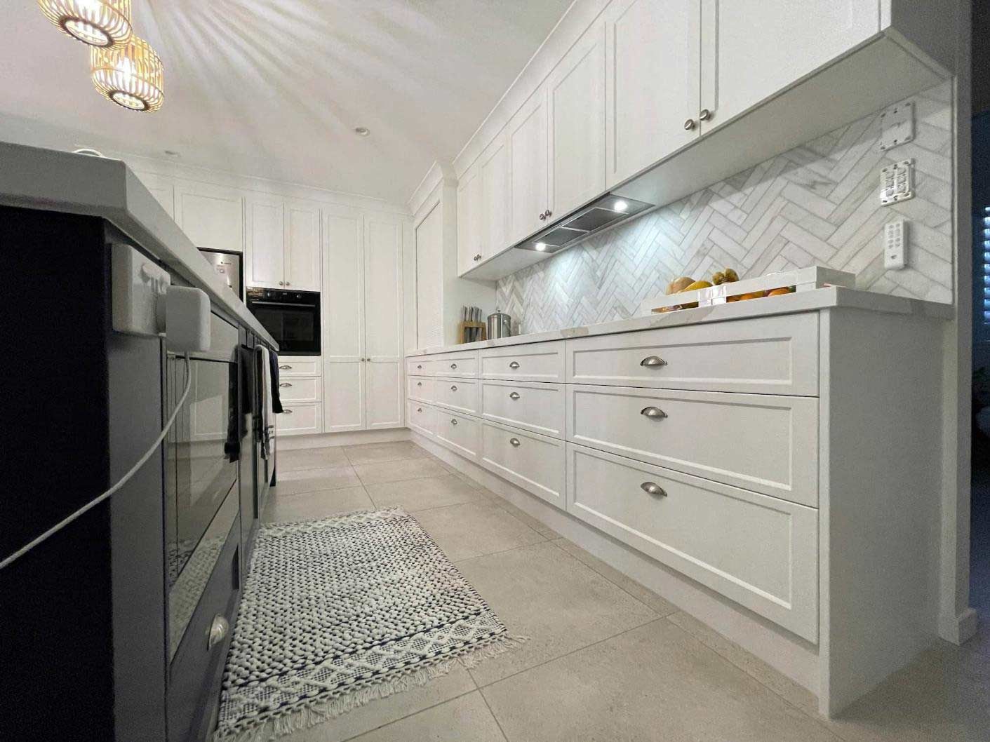 A Kitchen With White Cabinets And Black Appliances And A Rug On The Floor — Nyblad Construction in Caloundra West, QLD