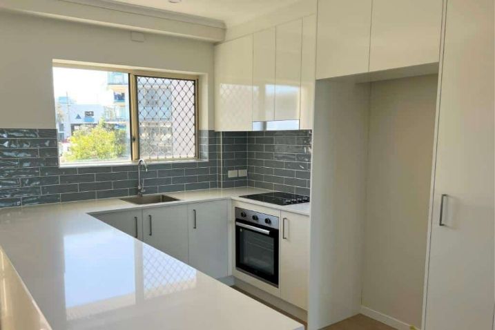 A Bright Kitchen With White Cabinets, A Sink, A Stove, And A Window — Nyblad Construction in Caloundra West, QLD
