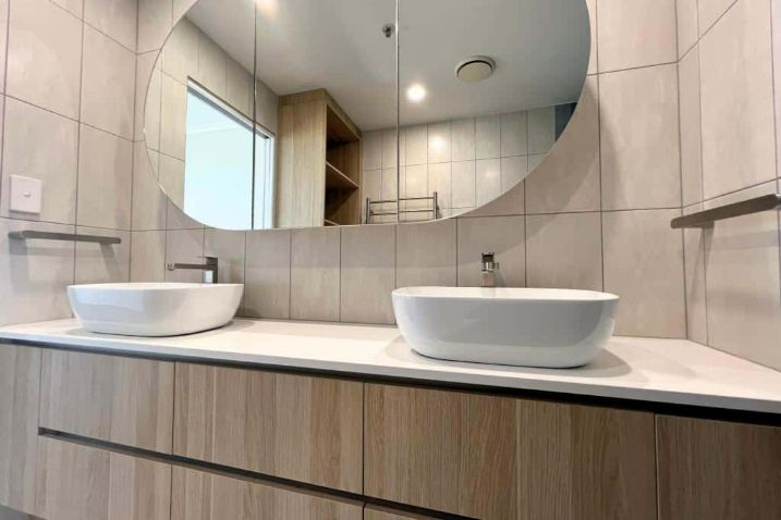 A Bathroom Designed With Two Sinks And A Circular Mirror — Nyblad Construction in Caloundra West, QLD