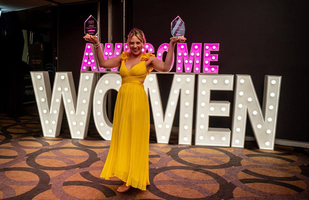 A Woman In A Yellow Dress Is Standing In Front Of A Large Sign — Nyblad Construction in Caloundra West, QLD
