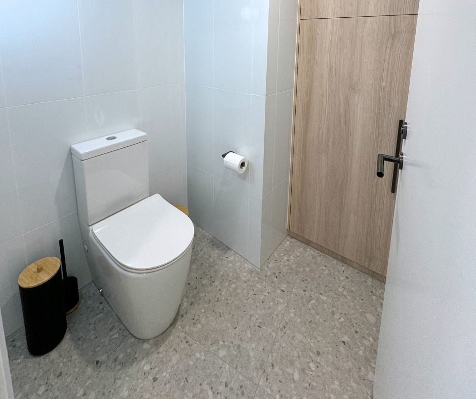 Modern bathroom with white toilet, speckled floor, and wooden door. — Nyblad Construction in Maroochydore, QLD