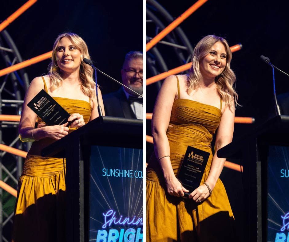 A Woman In A Yellow Dress Is Standing At A Podium Holding An Award — Nyblad Construction in Caloundra West, QLD