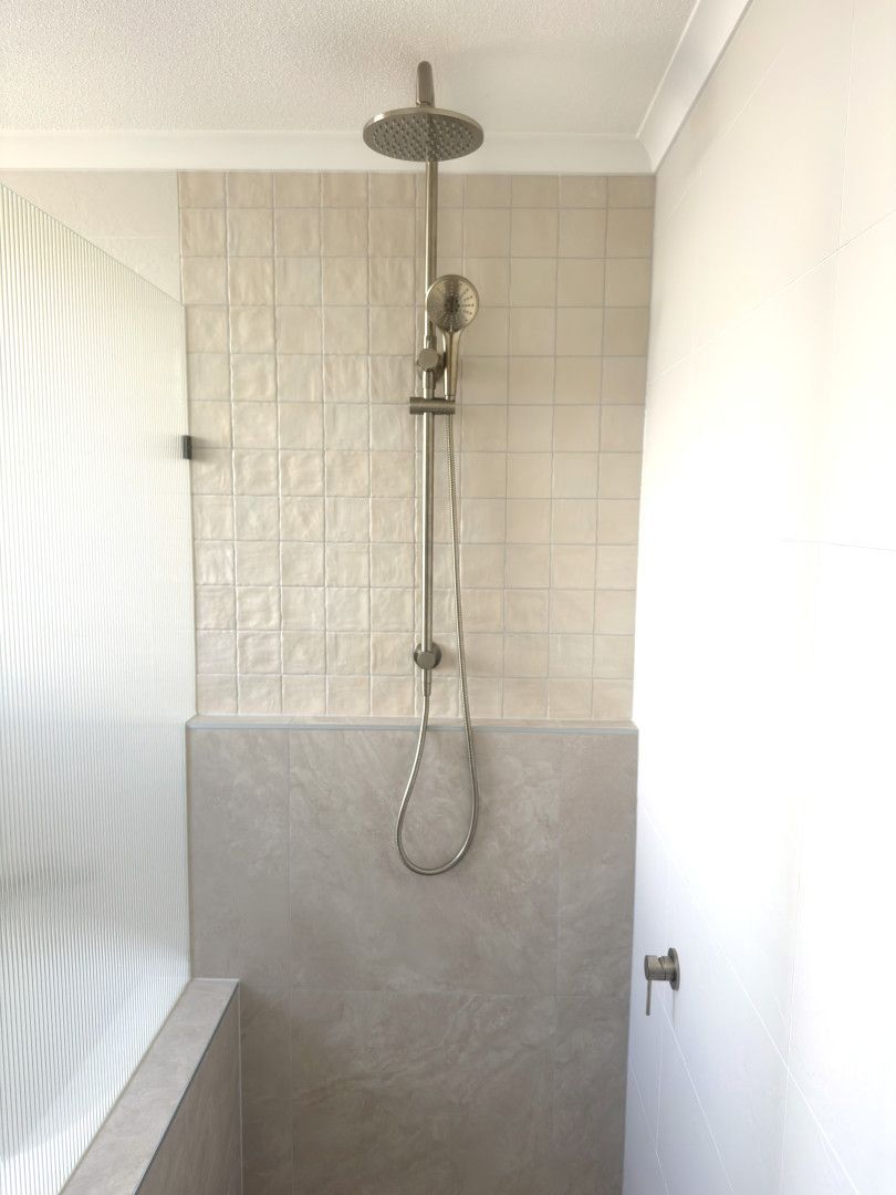 Shower stall with gray concrete lower wall, light textured tile above, and a silver shower head and handheld. — Nyblad Construction in Maroochydore, QLD