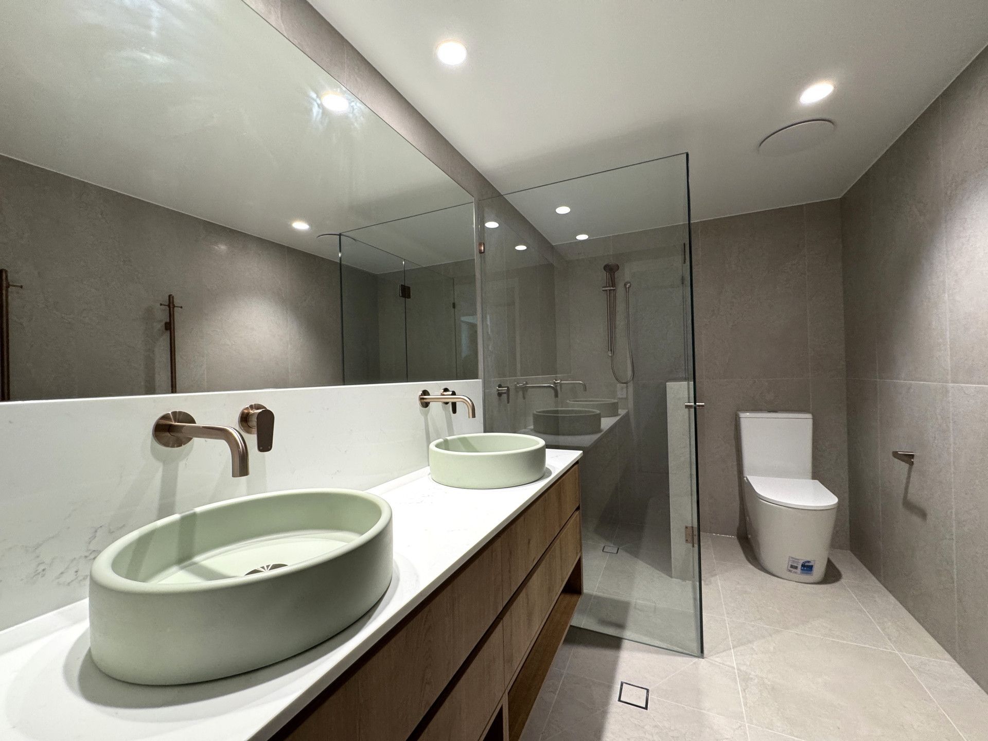 Modern bathroom with two green sinks, a glass shower, toilet, and large mirror. — Nyblad Construction in Maroochydore, QLD