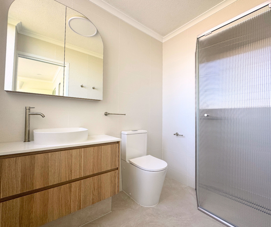 Modern Bathroom With Wood Vanity, White Sink, Toilet, and Glass Shower Door — Nyblad Construction in Caloundra West, QLD