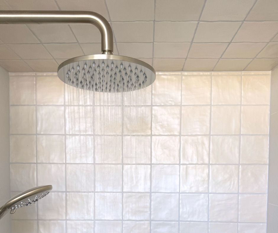 Showerhead With Water Spraying, Set Against White Tiled Wall — Nyblad Construction in Caloundra West, QLD